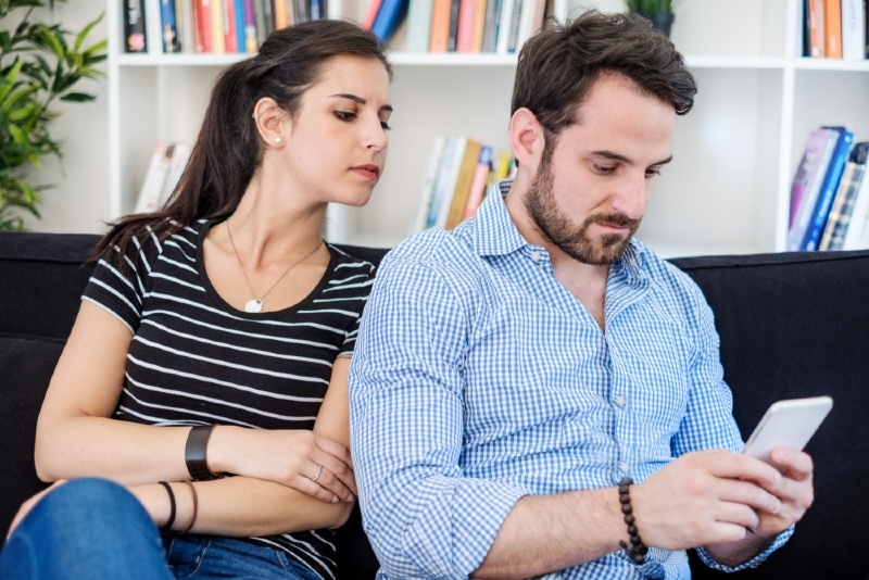 jealous woman looking at man's phone while sitting on sofa