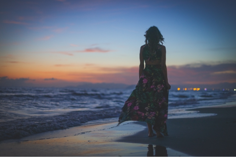 mujer con vestido largo de flores mirando al mar