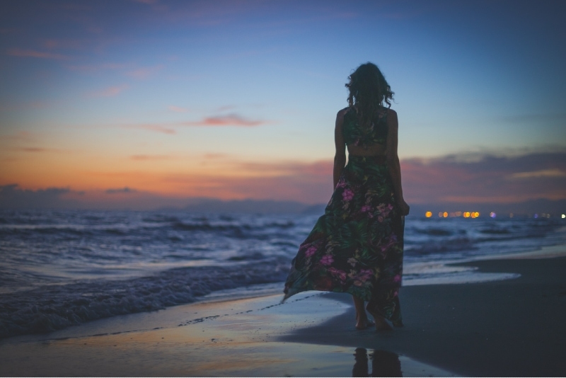 mulher com vestido longo floral a olhar para o mar