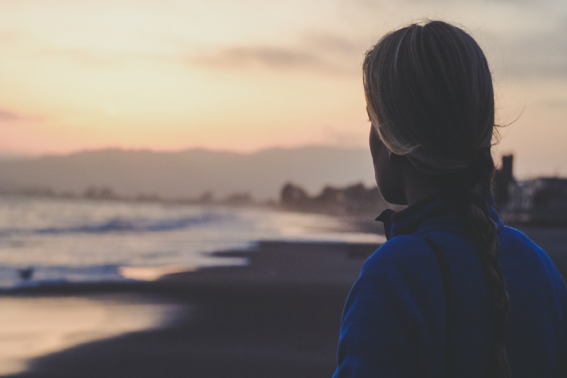 woman in blue jacket looking at sea during sunset