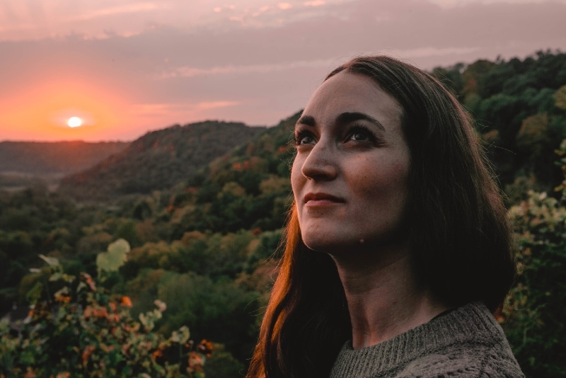 mujer mirando hacia arriba mientras está de pie al aire libre durante la puesta de sol