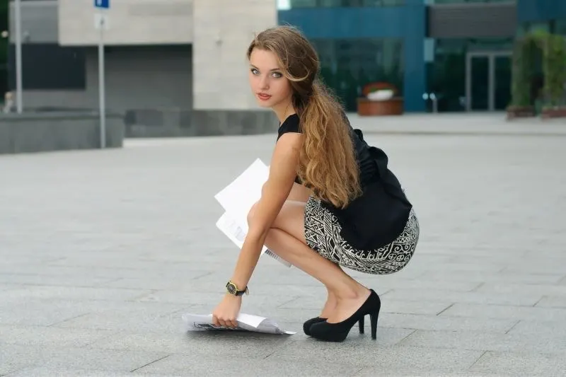woman picking up some documents that fell of the ground outside a building