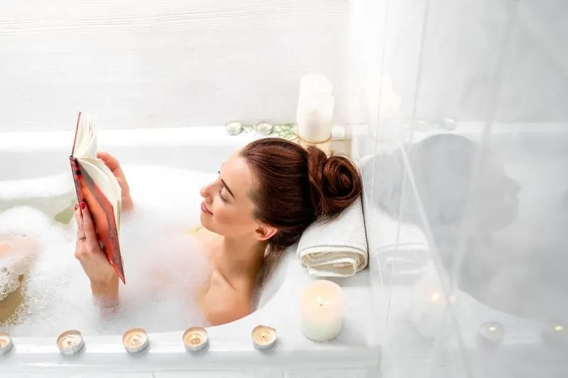 woman relaxing and reading a book at the bath tub surrounded with candles