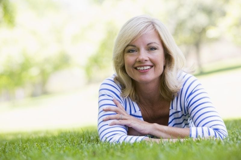 donna che si rilassa all'aperto sdraiata sull'erba verde sorridendo alla telecamera