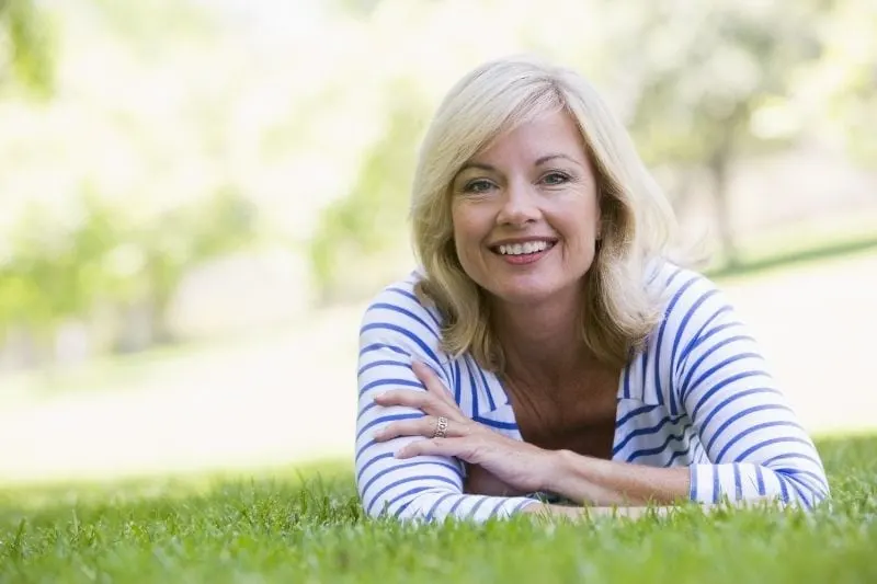 woman relaxing outdoors lying down on the green grass smiling at the camera