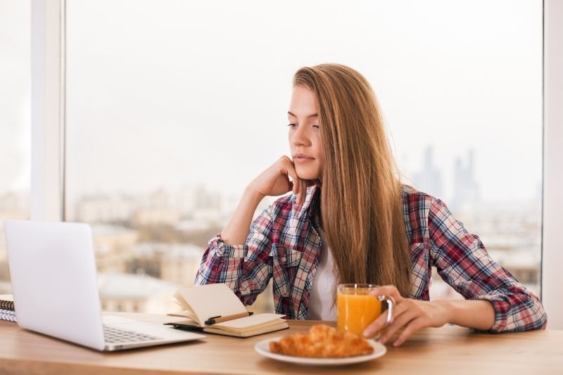 woman sat by the table with snacks and looking at the laptop and notebook