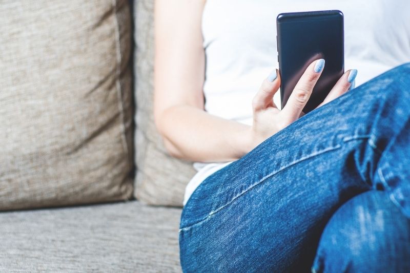 mulher sentada num sofá segurando um telemóvel em imagem recortada