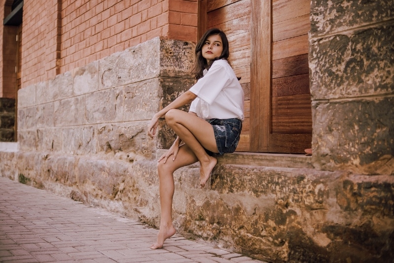 mulher de camisa branca sentada perto de um velho edifício de pedra