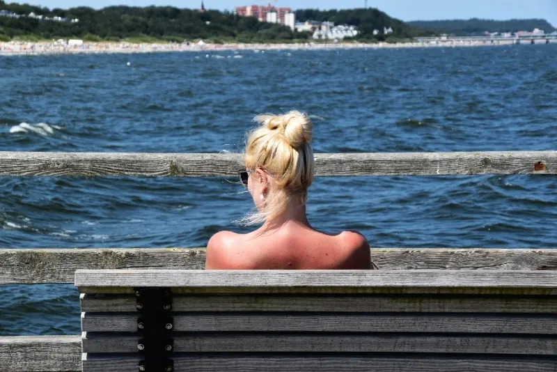 blonde woman sitting on bench looking at sea