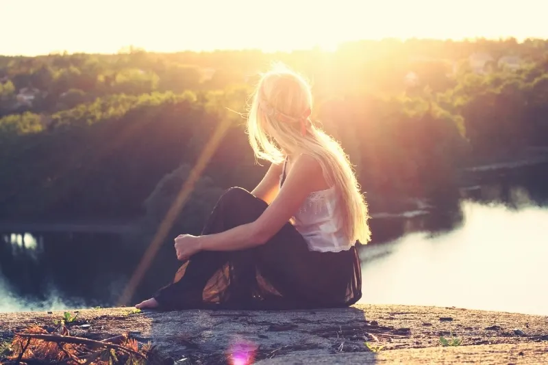 blonde woman sitting on ground looking at river