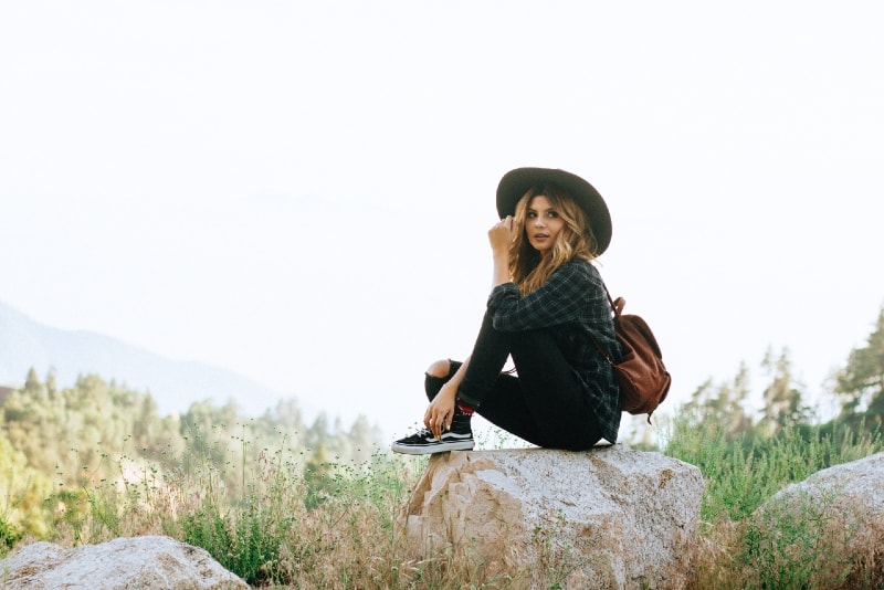 donna con cappello nero seduta su una roccia