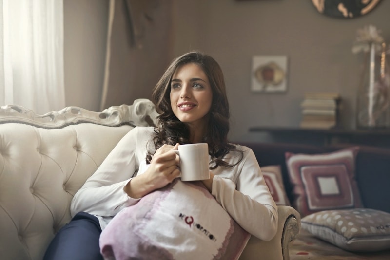 woman holding white mug while sitting on sofa