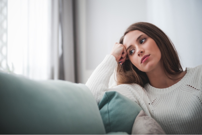 mujer triste con jersey blanco sentada en un sofá