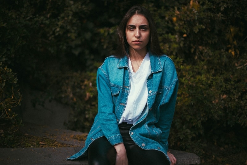donna arrabbiata con giacca di jeans seduta su una pietra