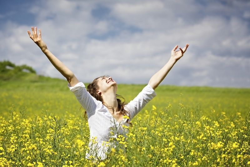 woman smiling and raise her hand in the middle of the flower field during the day