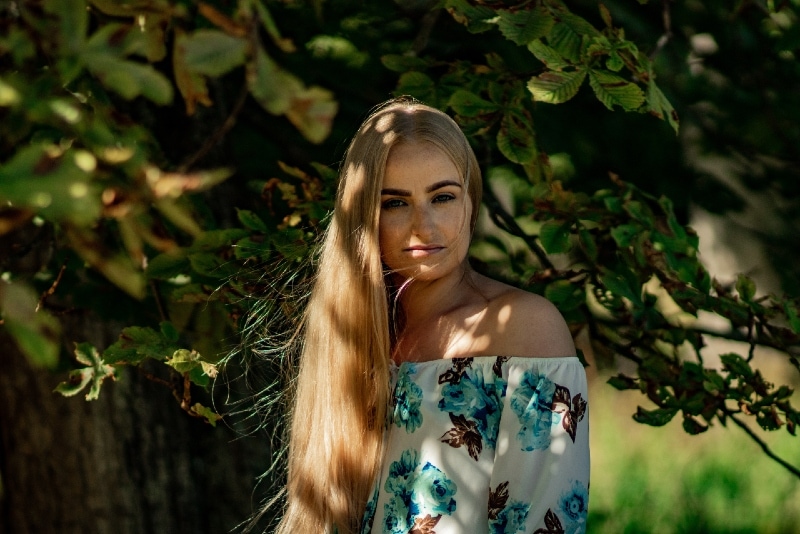 blonde woman in floral top standing near tree