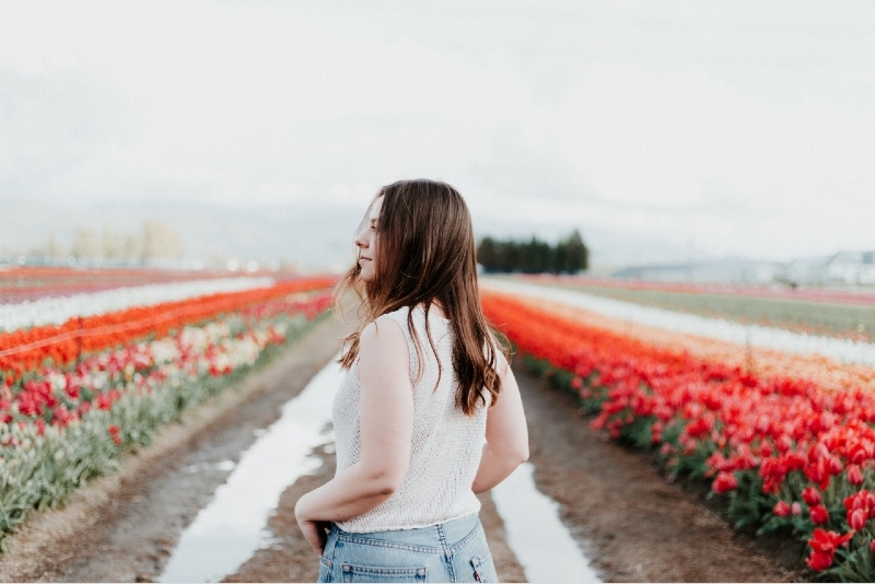 woman in white top standing near red tulips