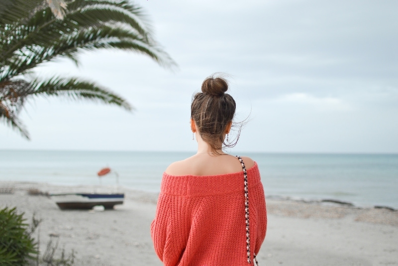 donna con maglione rosso in piedi sulla spiaggia