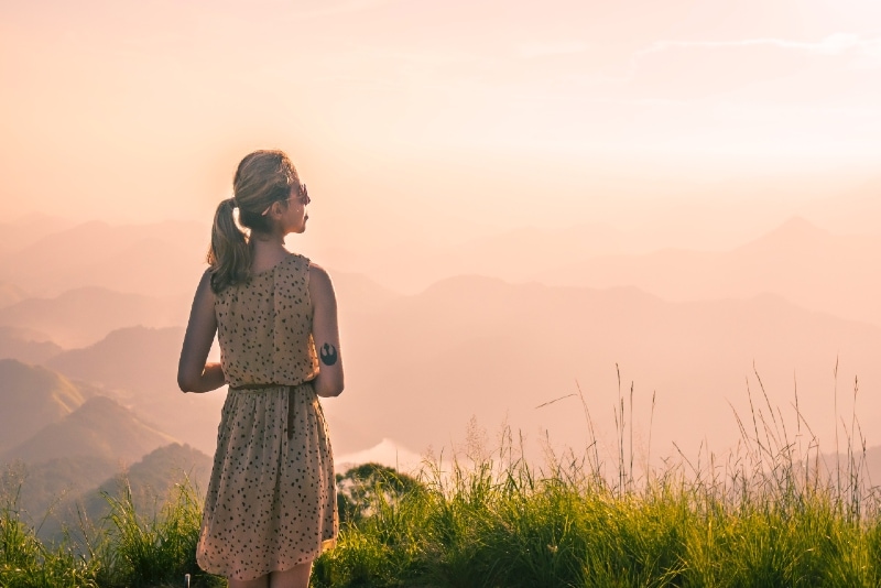 mujer de pie sobre la hierba mirando a la montaña