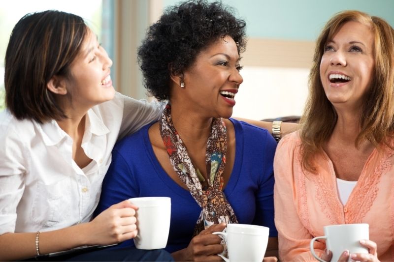 mulher a conversar e a rir-se com outras mulheres enquanto segura chávenas de café