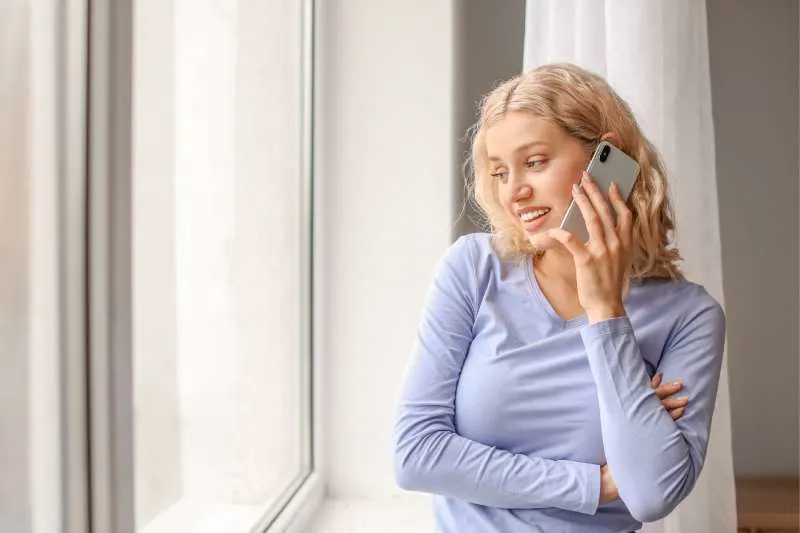 woman talking on phone inside home standing near the glass windows