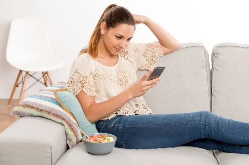 woman texting beside a food in a bowl in the sofa