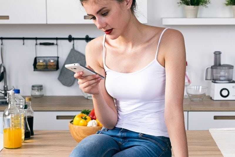 woman using cellphone sitting on the kitchen's wooden centertop