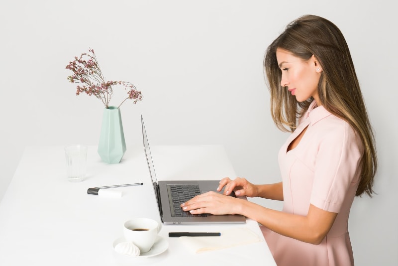woman in pink dress using laptop while sitting at table