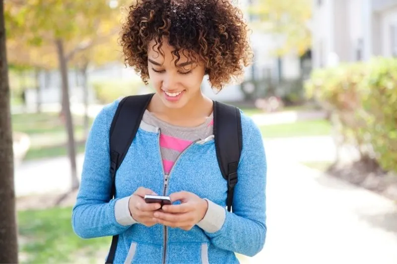 woman with curly hair with a backpack texting inside the university