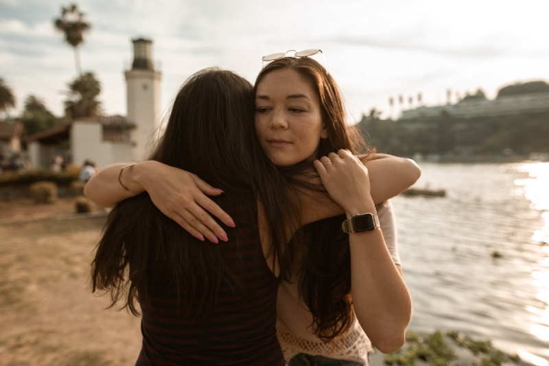 two women hugging while standing near water