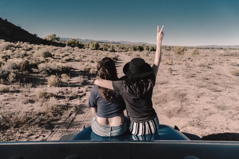 two women hugging while sitting on car hood