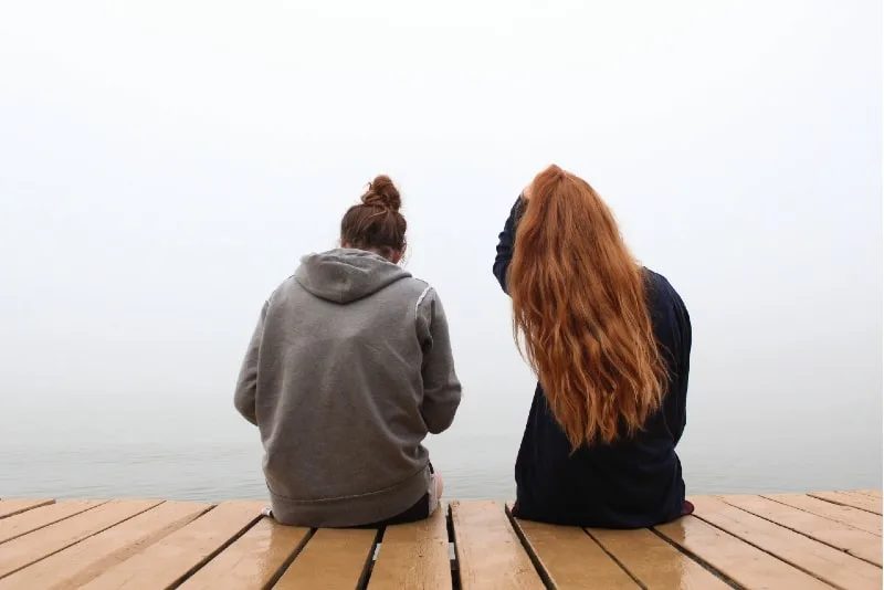 two women sitting on wooden dock near water