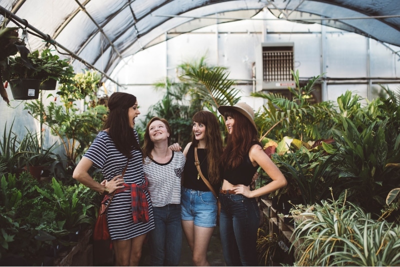 four women hugging while standing near plants