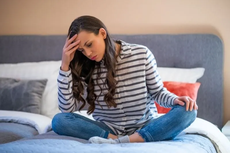 worried pensive woman sitting on the bed with hand supporting her head