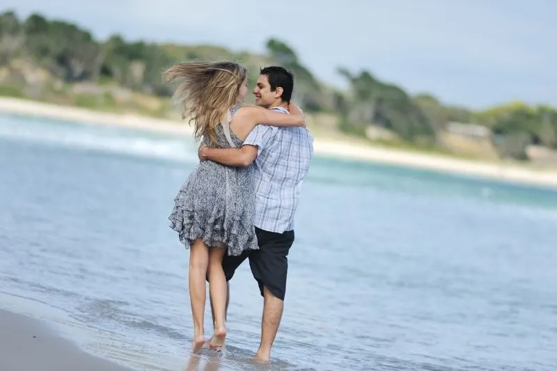 young couple at the beach hugging while taking a walk during a hot weather