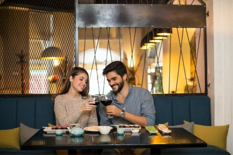 young couple drinking wine inside the restaurant sitting next to each other