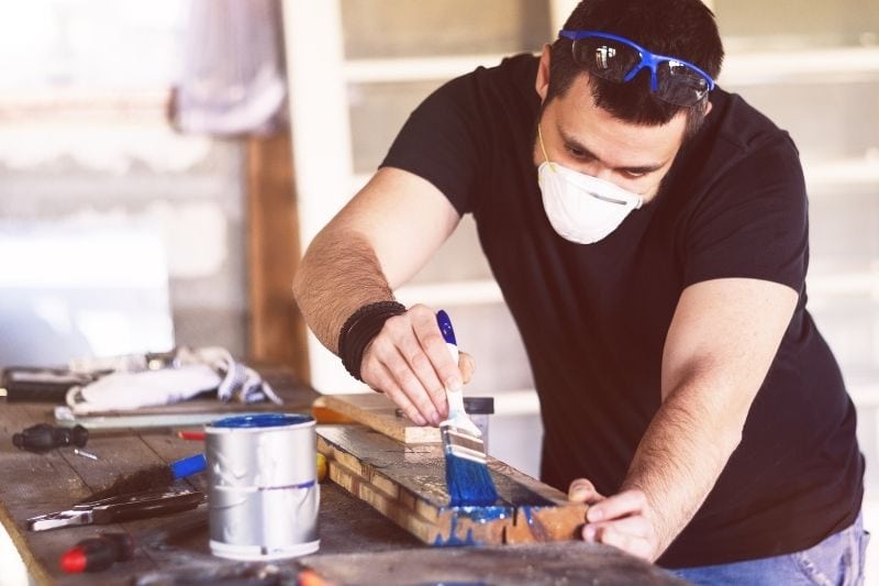 young man painting a wooden slab with blue