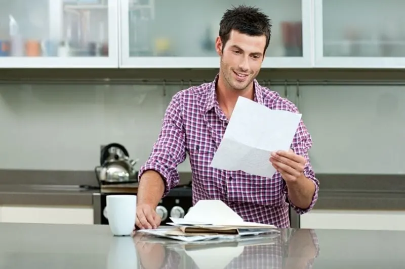 young man reading letter in the kitchen with papers in the countertop
