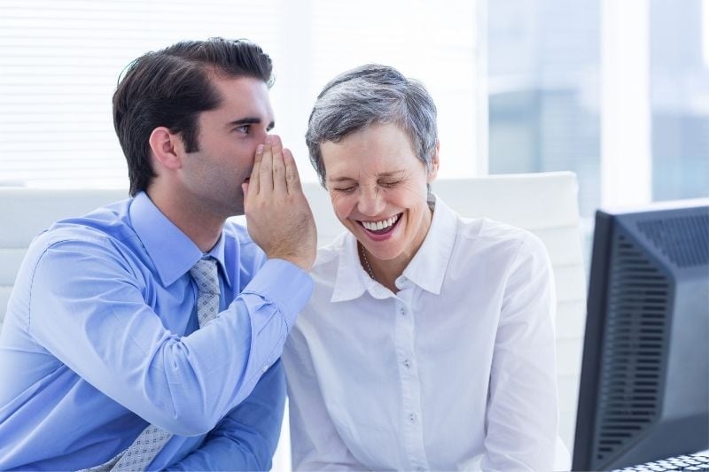 young man whispers to the mature colleague and made her laugh hard 