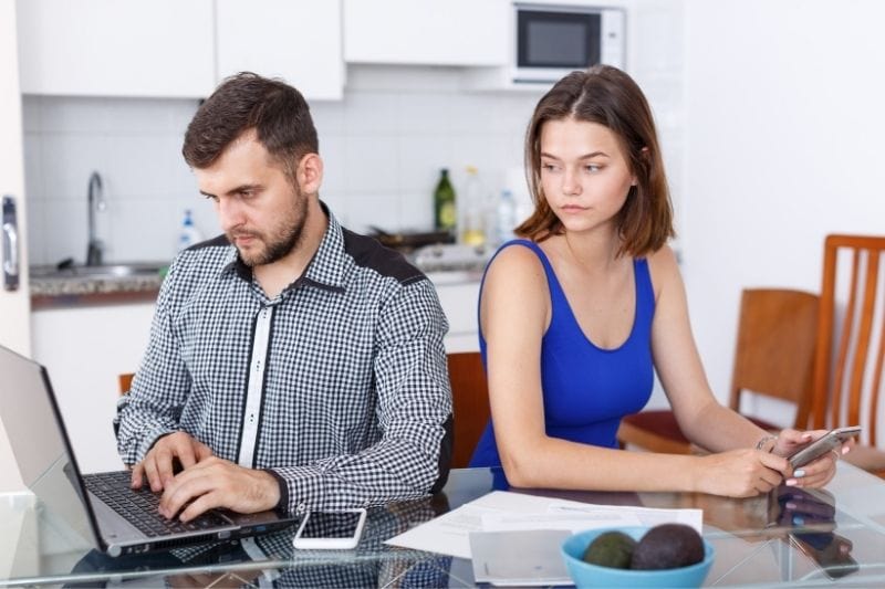 young man working on laptop with an upset woman looking at his laptop sitting beside him at the table
