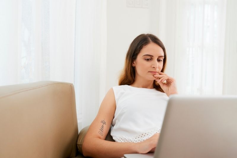 giovane donna pensierosa che lavora al suo laptop all'interno di un ufficio al suo tavolo