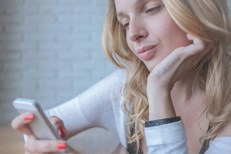 young pensive woman texting on her smartphone while one hand supporting her chin