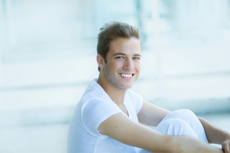 young pretty man looking at the camera sitting wearing white shirt and white trousers