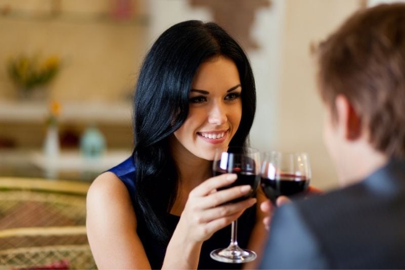 joven mujer romántica teniendo una cita con un chico sonriendo y sosteniendo una copa de vino