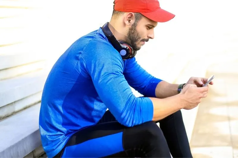 young smiling man wearing athletic wear and sitting in a bench texting