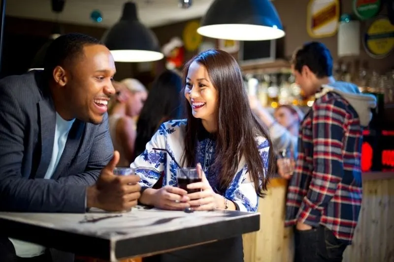 young woman chatting to a man in bar with a drink on their table