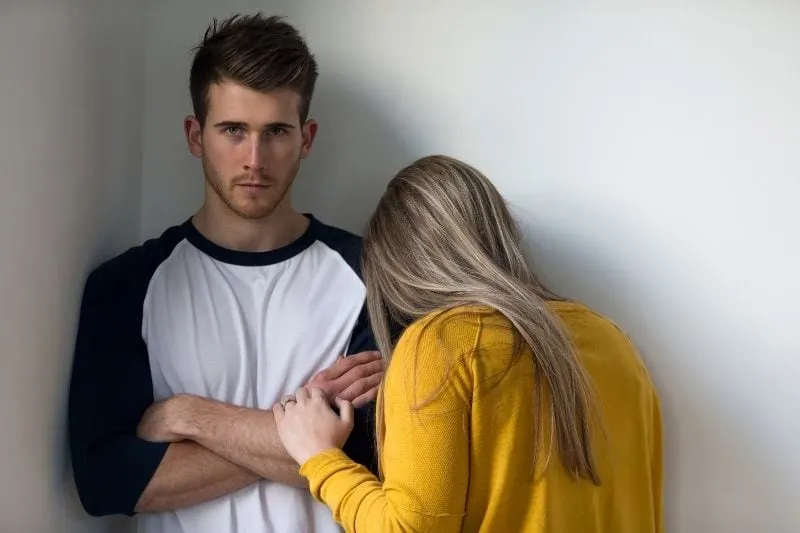 young woman crying over man's shoulder while man looking stiff at the camera