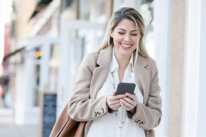 young woman laughs while reading the text message while walking outdoors