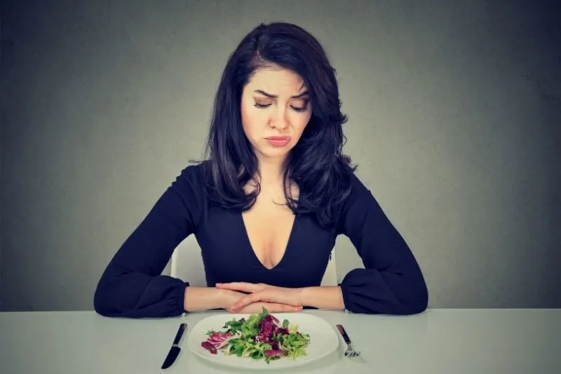 young woman looking at the plate with desperate expression 