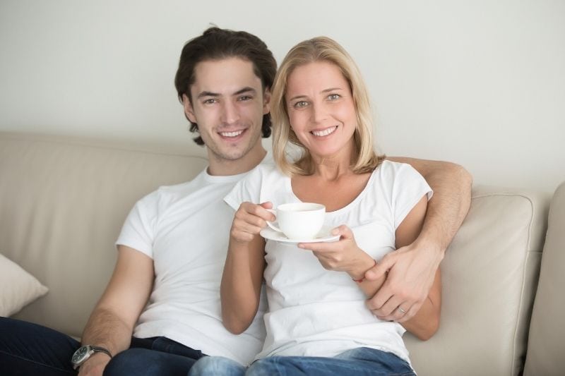hombre joven abrazando a una mujer madura tomando cafe en el sofa